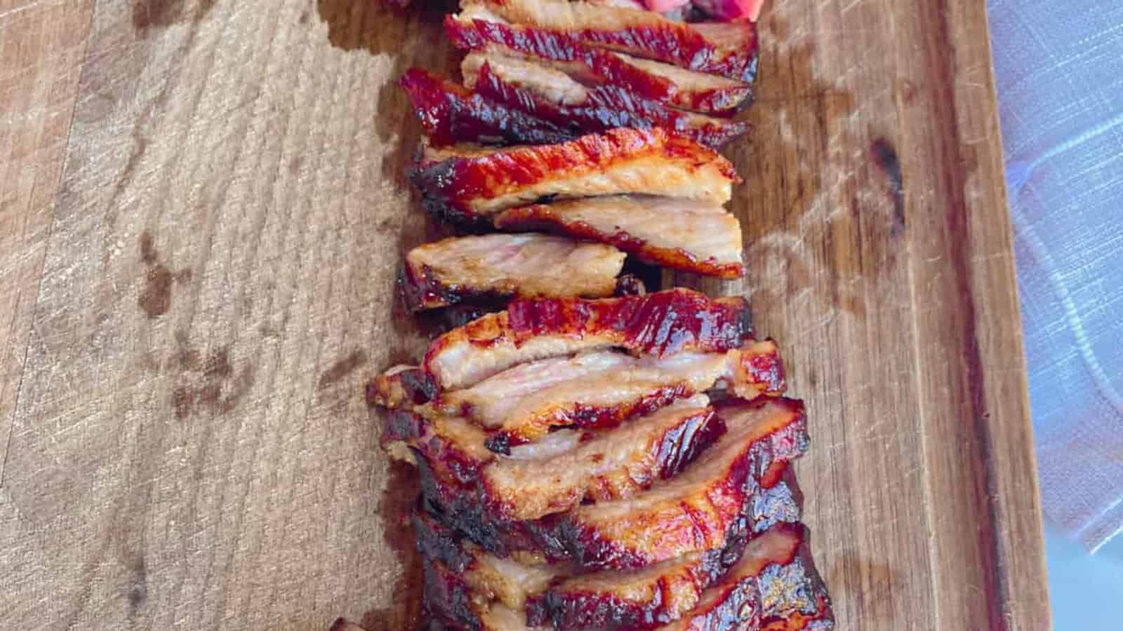 Tender and juicy Chinese BBQ pork slices on a brown wooden cutting board.