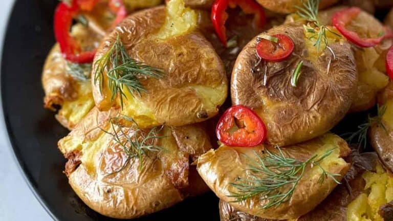 Closeup of crispy smashed potatoes with dill and chili slices