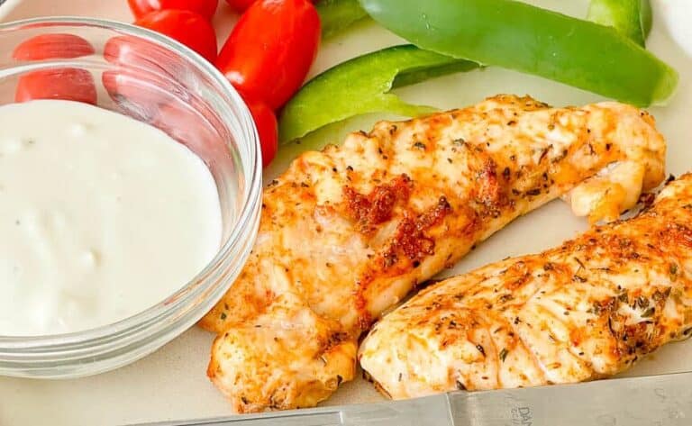 Golden and crispy air fryer chicken tenders served on a white plate with a side of dipping sauce, perfect for a quick and delicious meal.