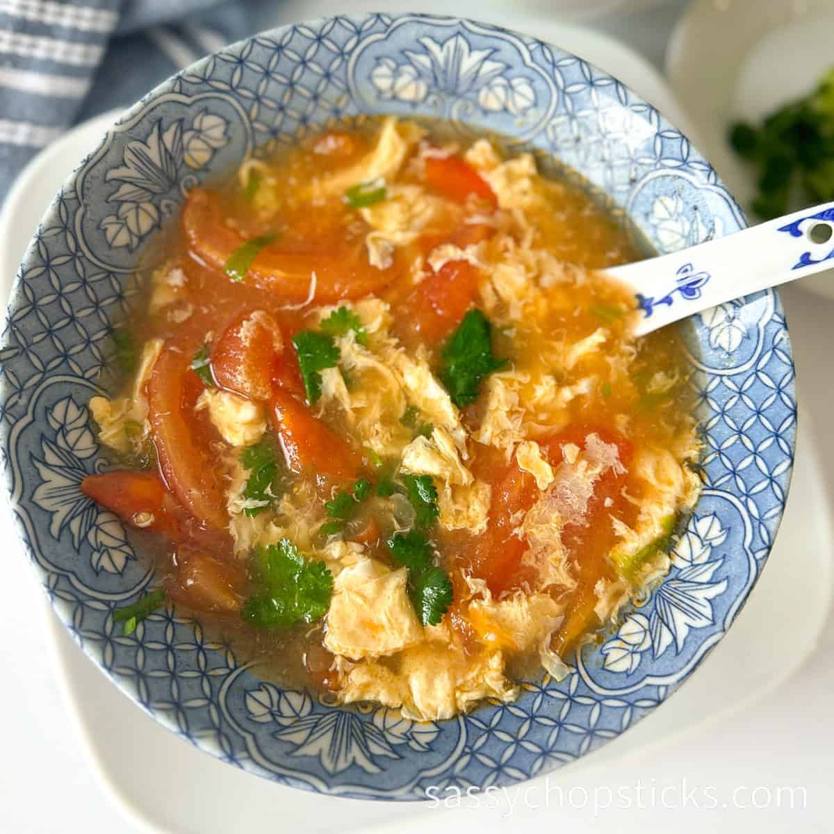 Tomato egg drop soup in a bowl with a blue white spoon.