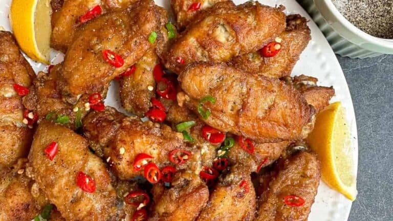 Crispy and flavorful salt and pepper chicken wings on a plate with lemon wedges.