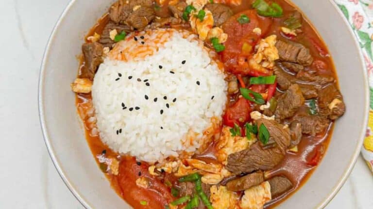 Savory tomato beef stir-fry with soft scrambled eggs with rice in a white bowl.