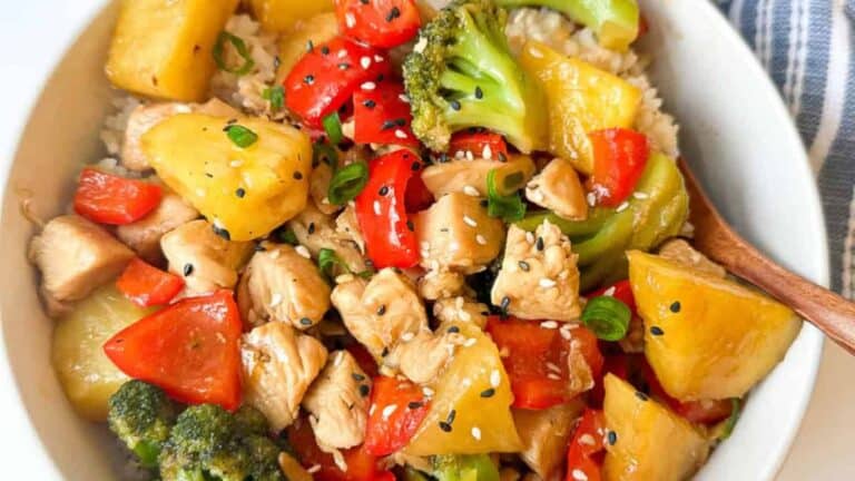 A vibrant bowl containing chicken, assorted vegetables, pineapple chunks, teriyaki sauce, and rice.