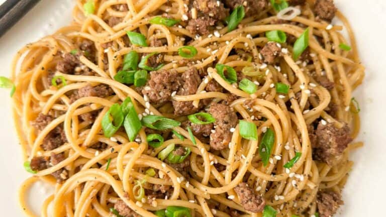 A plate of Chinese Mongolian beef noodles garnished with fresh green onions and roasted sesame seeds.