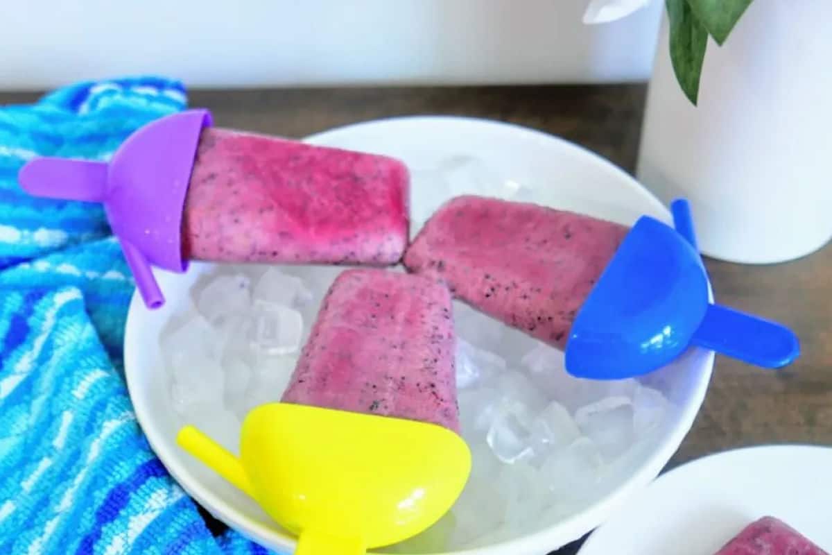 Homemade blueberry popsicles with colorful handles on a plate of ice.