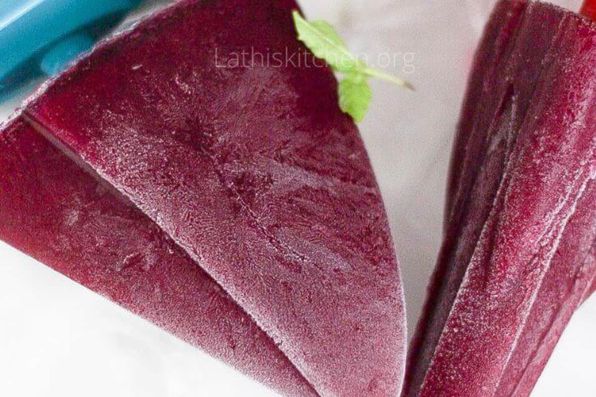 Deep purple plum popsicles with a smooth texture rest on a white surface, accompanied by a sprig of mint.