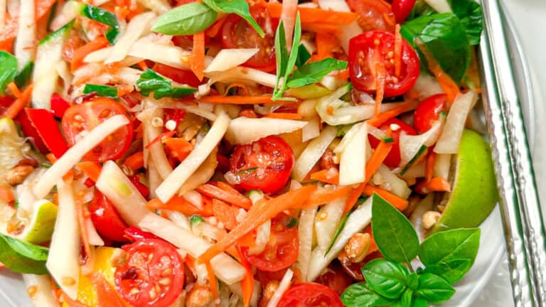 A colorful plate of fresh vietnamese salad featuring vibrant carrots, juicy tomatoes, and green papaya.