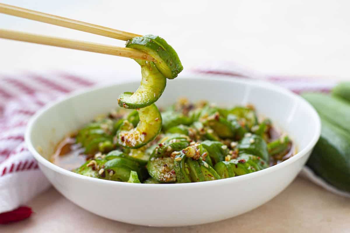 A bowl featuring pickled cucumbers and chopsticks.