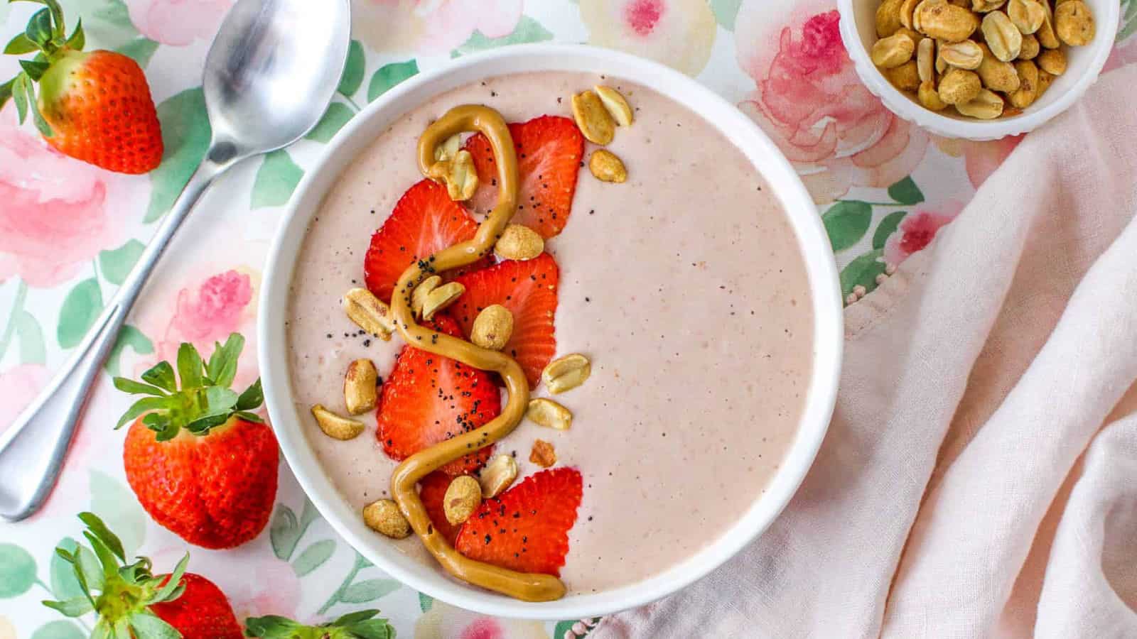 Smoothie topped with strawberries, peanuts, and peanut butter swirl in bowl.