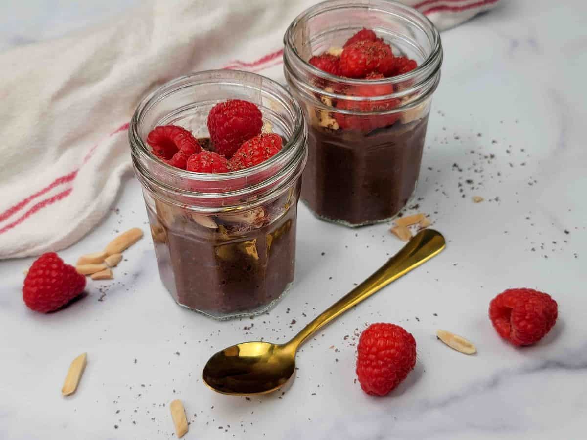 Two jars of chocolate pudding with raspberries and almonds.