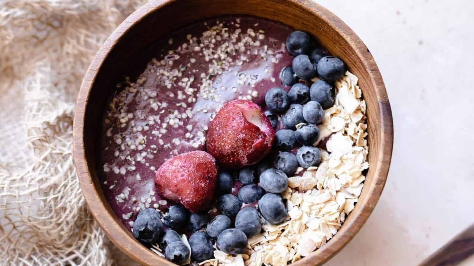 Açaí berries topped with fresh fruit, granola, and seeds in a brown bowl.