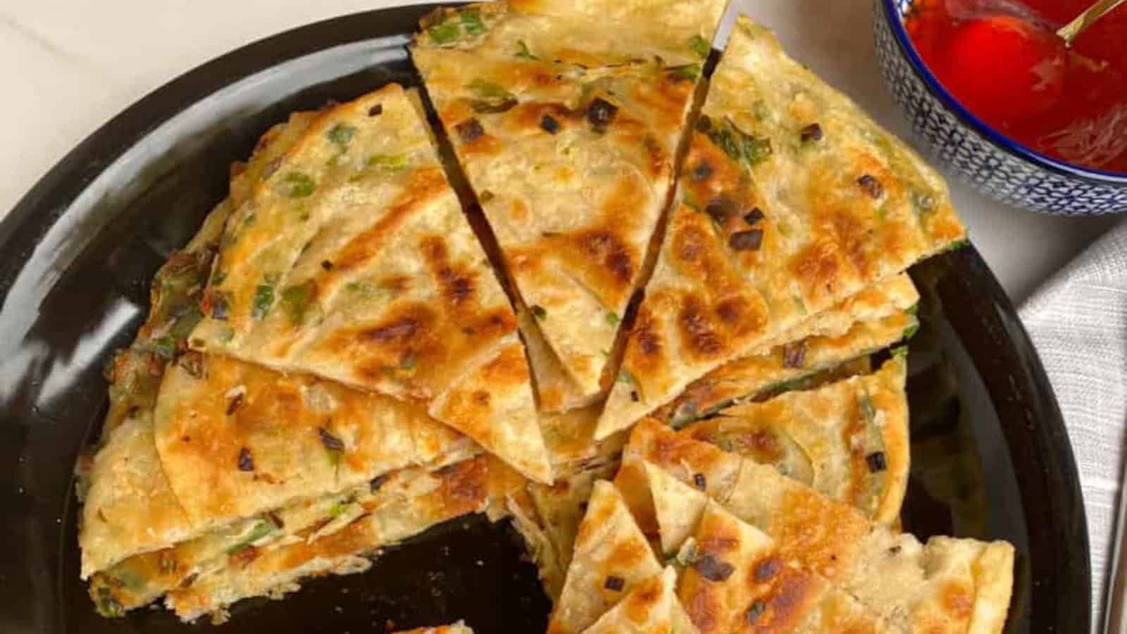 Flaky and crispy Chinese scallion pancakes on a black plate.