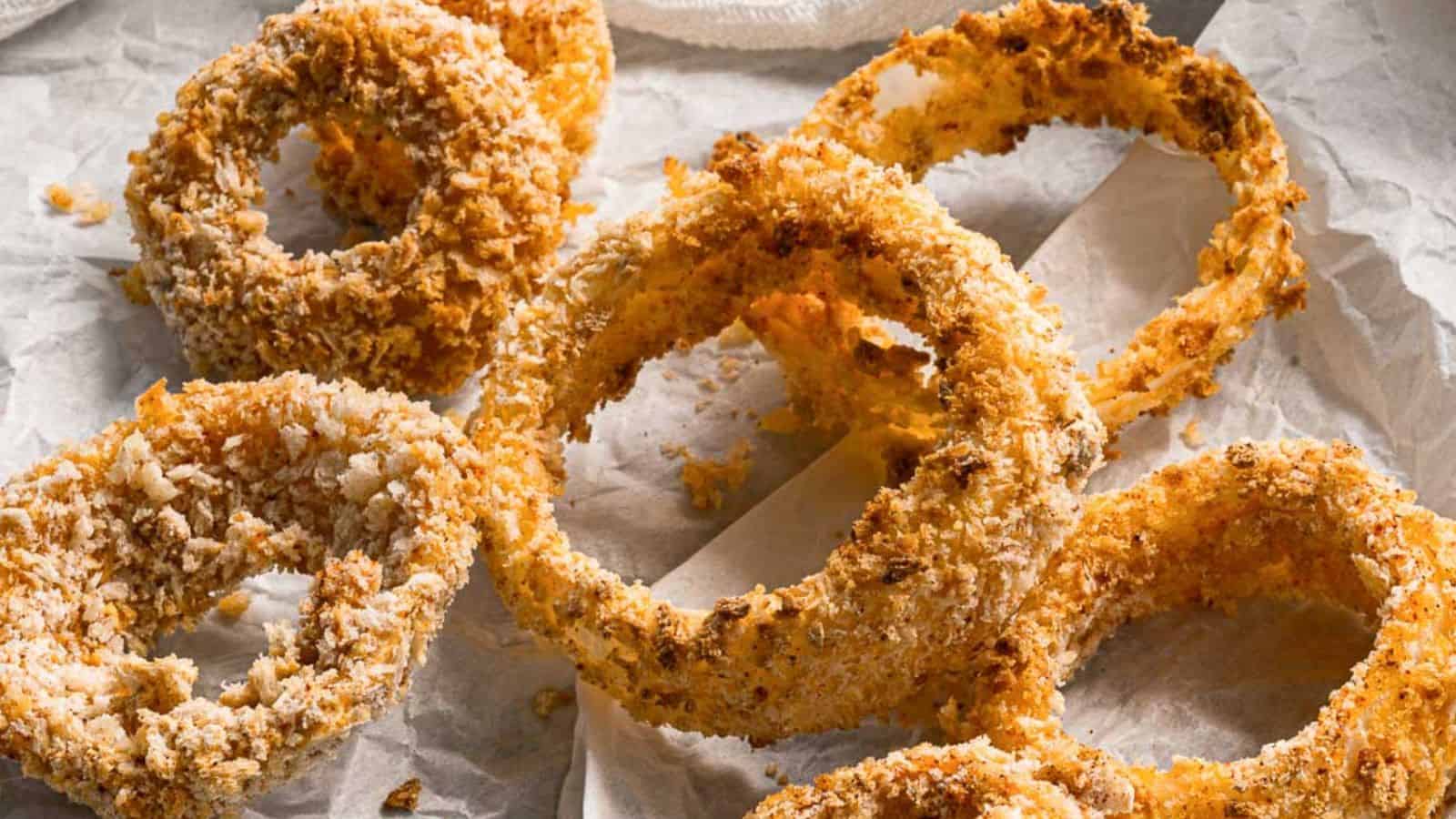 A plate of crispy, golden-brown air fryer onion rings, served on parchment paper with a dipping sauce on the side.
