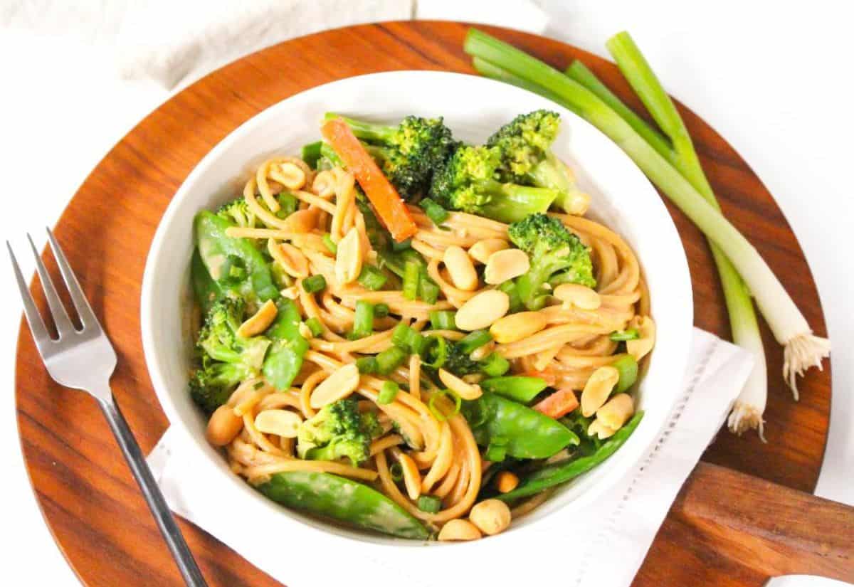 A bowl with spaghetti pasta, broccoli, snap peas, carrots, and peanuts tossed in peanut sauce.