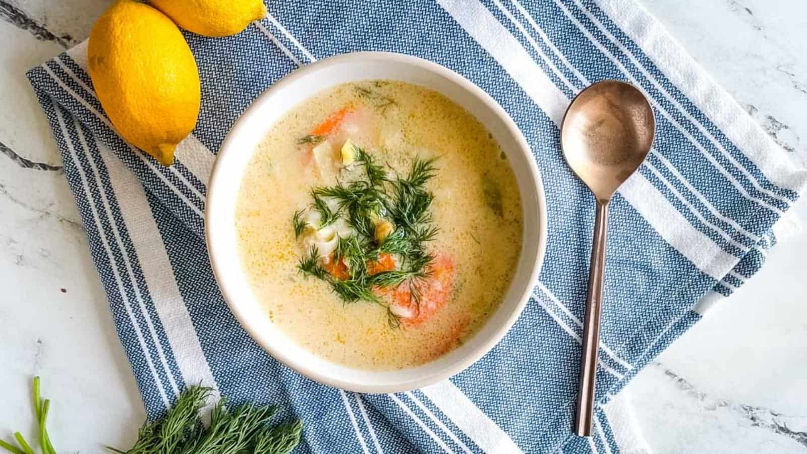 A bowl of Greek chickpea soup garnished with dill on a blue and white linen with a gold spoon.