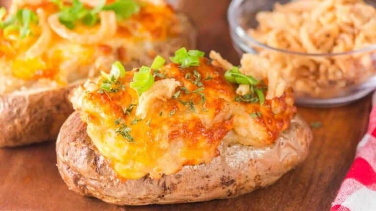 Loaded baked potatoes topped with melted cheese, green onions, and crispy fried onions, served on a wooden surface with a small bowl of more crispy onions in the background.