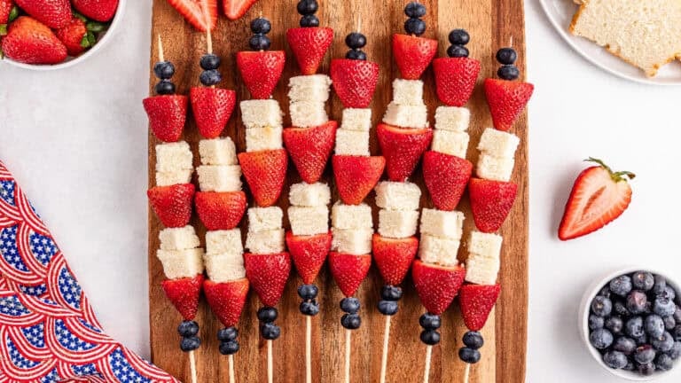 A wooden cutting board displaying assortment of strawberries,pound cake pieces, and blueberries.