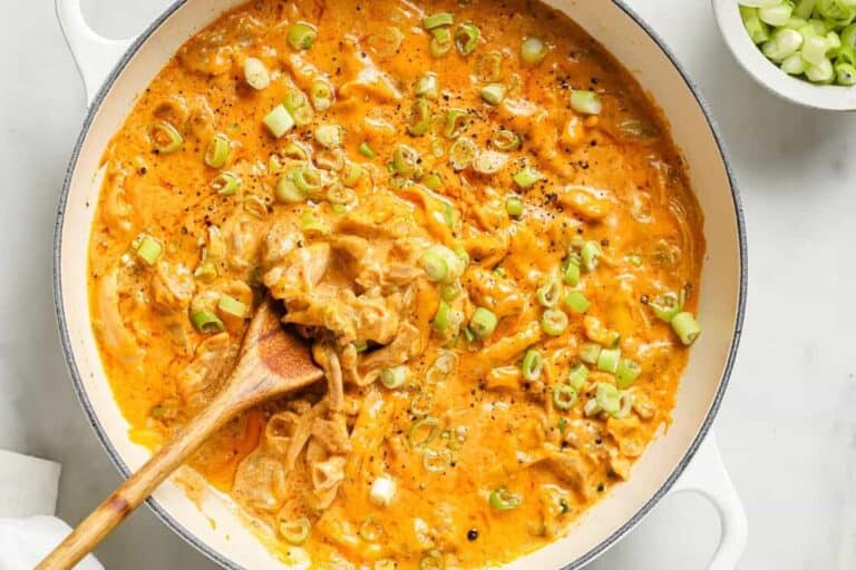 Green chile chicken in a pan with a wooden spoon.