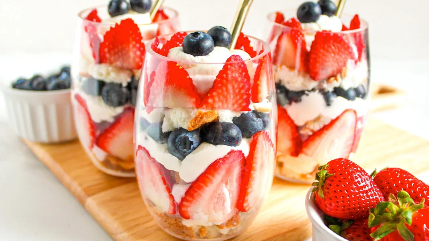 A festive red, white, and blue mini trifle featuring layers of angel food cake, homemade whipped cream, fresh strawberries, and blueberries, served in individual cups for easy enjoyment.
