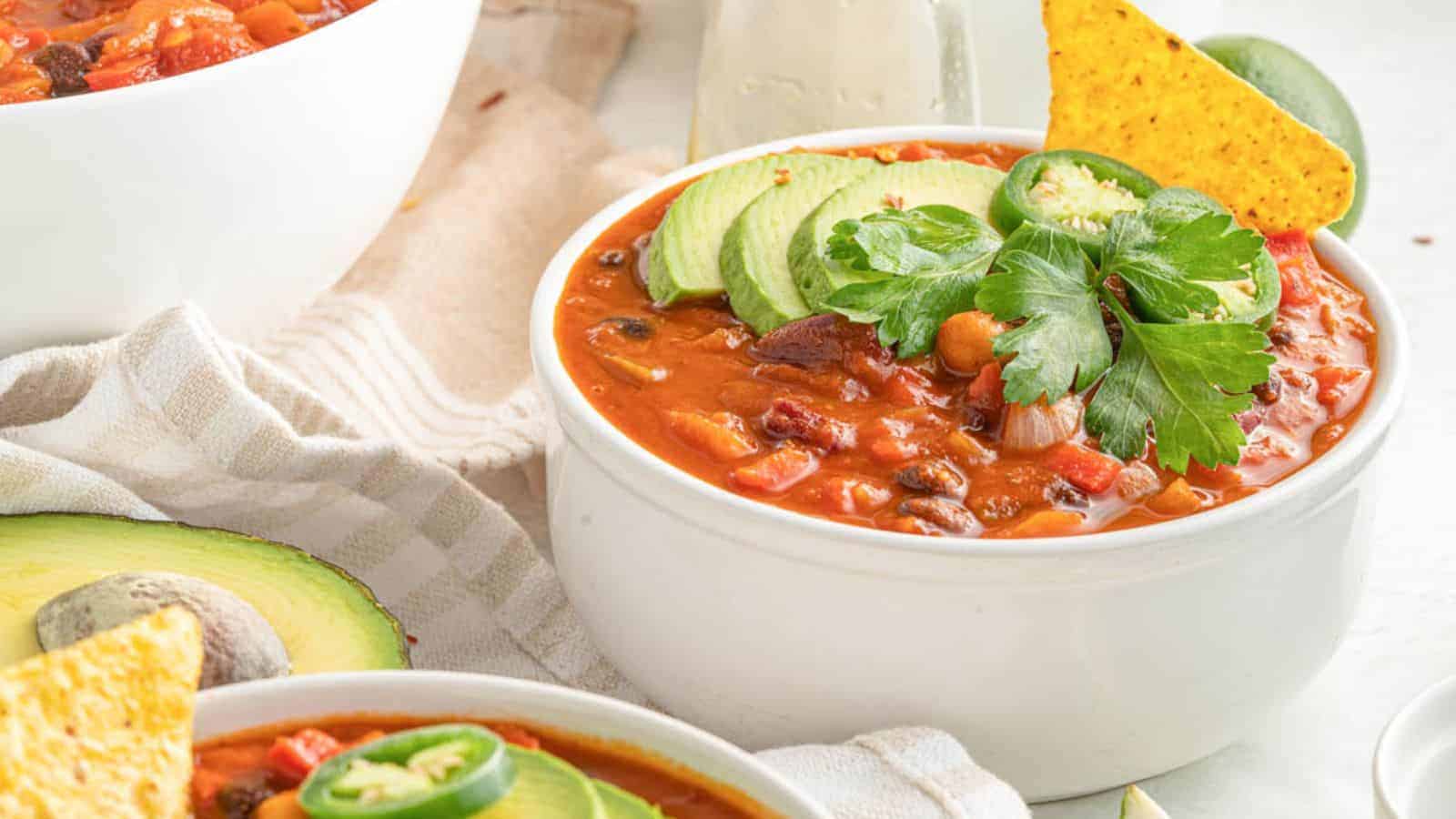 A hearty bowl of mixed bean chili with a rich tomato base and colorful beans, garnished with herbs.