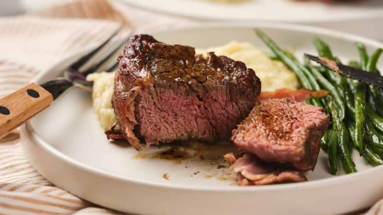 A plate with a cooked steak cut into pieces, accompanied by mashed potatoes and green beans.
