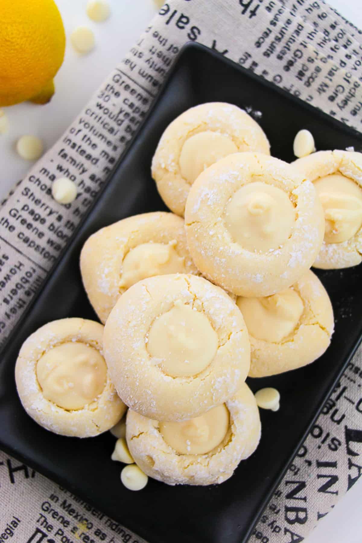 A plate of lemon cookies displayed on a newspaper, with lemons nearby.