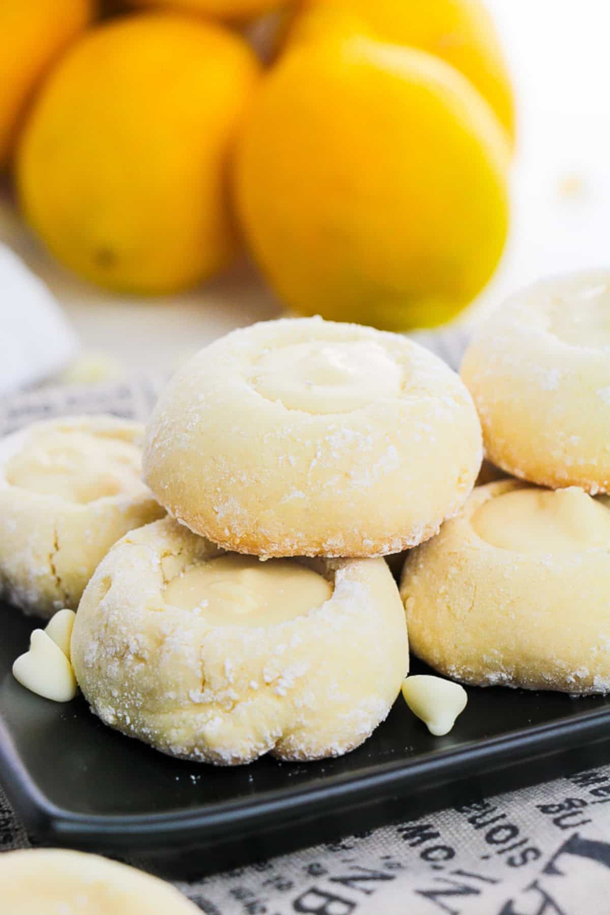 A plate of lemon cookies displayed on a newspaper, with lemons nearby closer view.