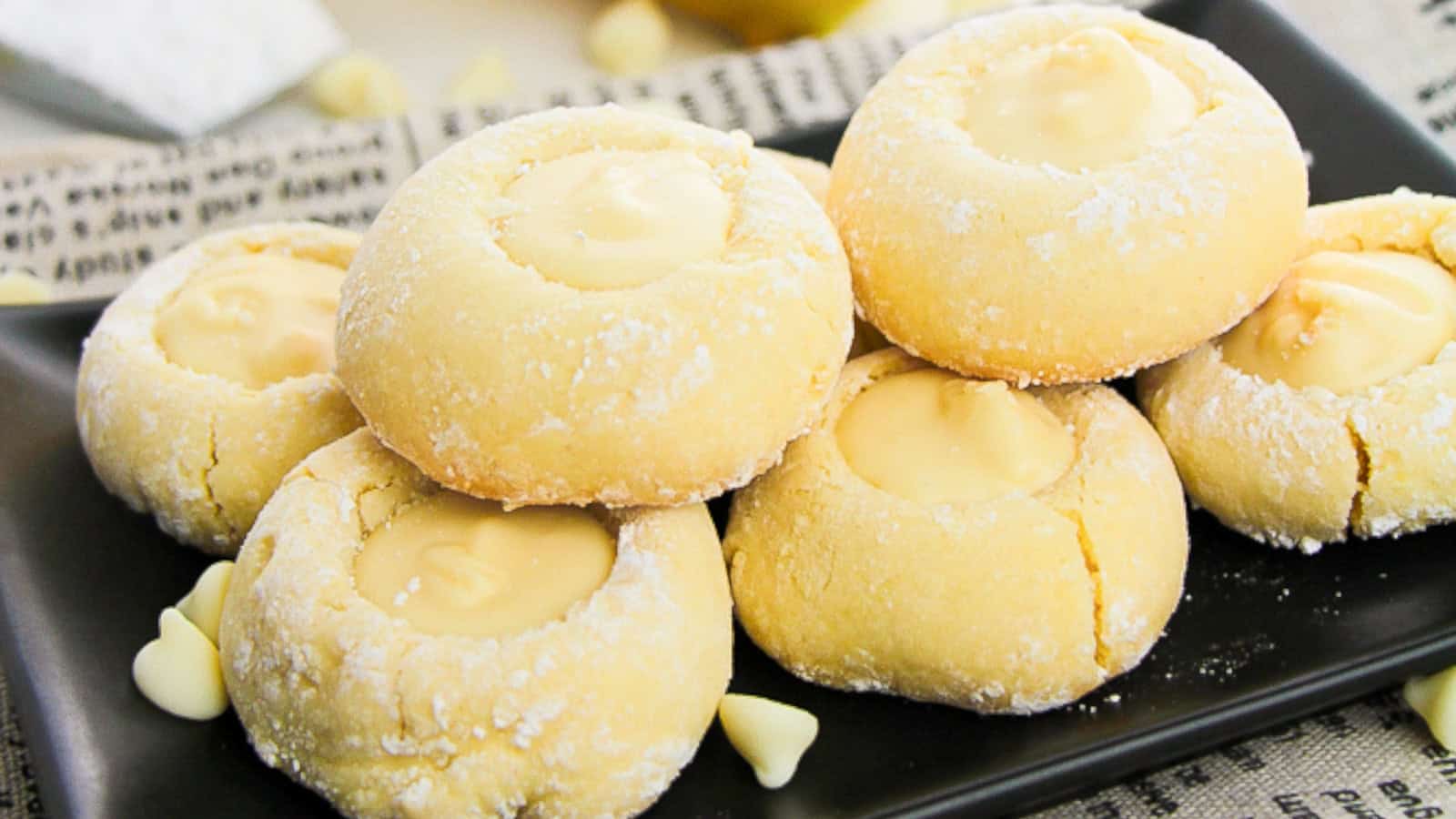 A plate of lemon cookies displayed on a newspaper, with a few lemons nearby.
