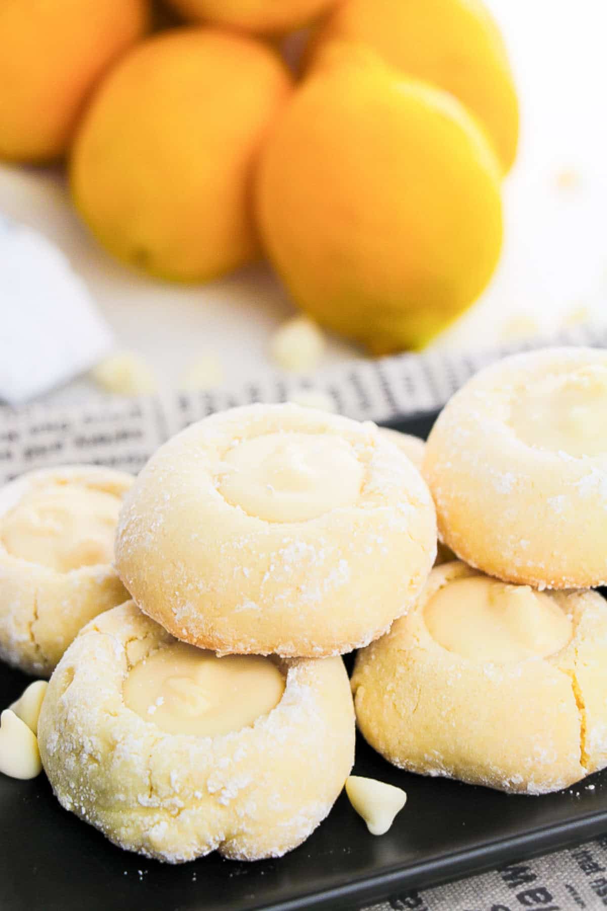 A plate of lemon cookies displayed on a newspaper, with lemons nearby.