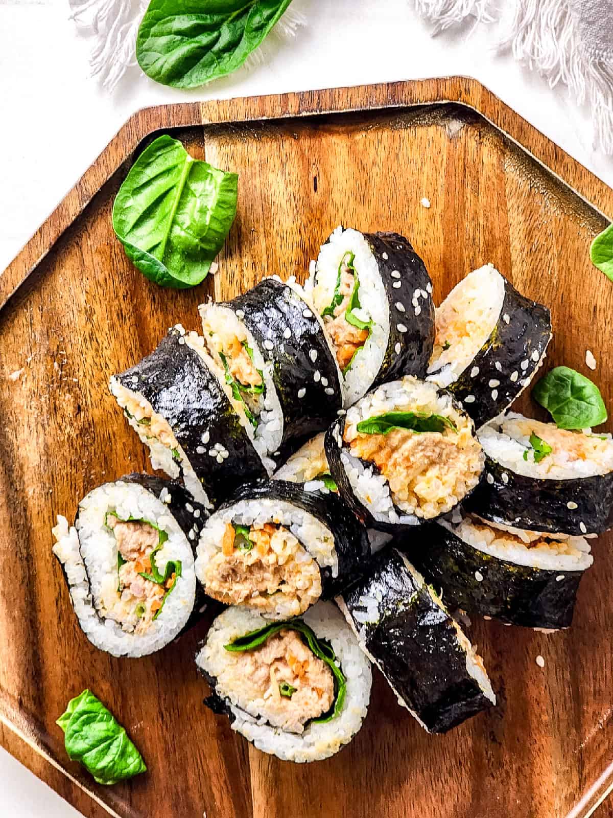 Tuna kimbap rolls on a brown wooden cutting board, featuring a mix of ingredients.