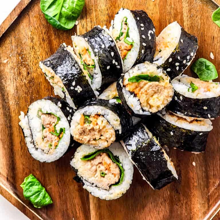 Tuna kimbap on a brown cutting board with a few spinach leaves on the side.