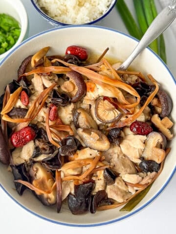 Homemade Chinese steamed chicken soup loaded with wood ear mushrooms, shiitake, dried lily buds, and served with steamed rice and green onions.