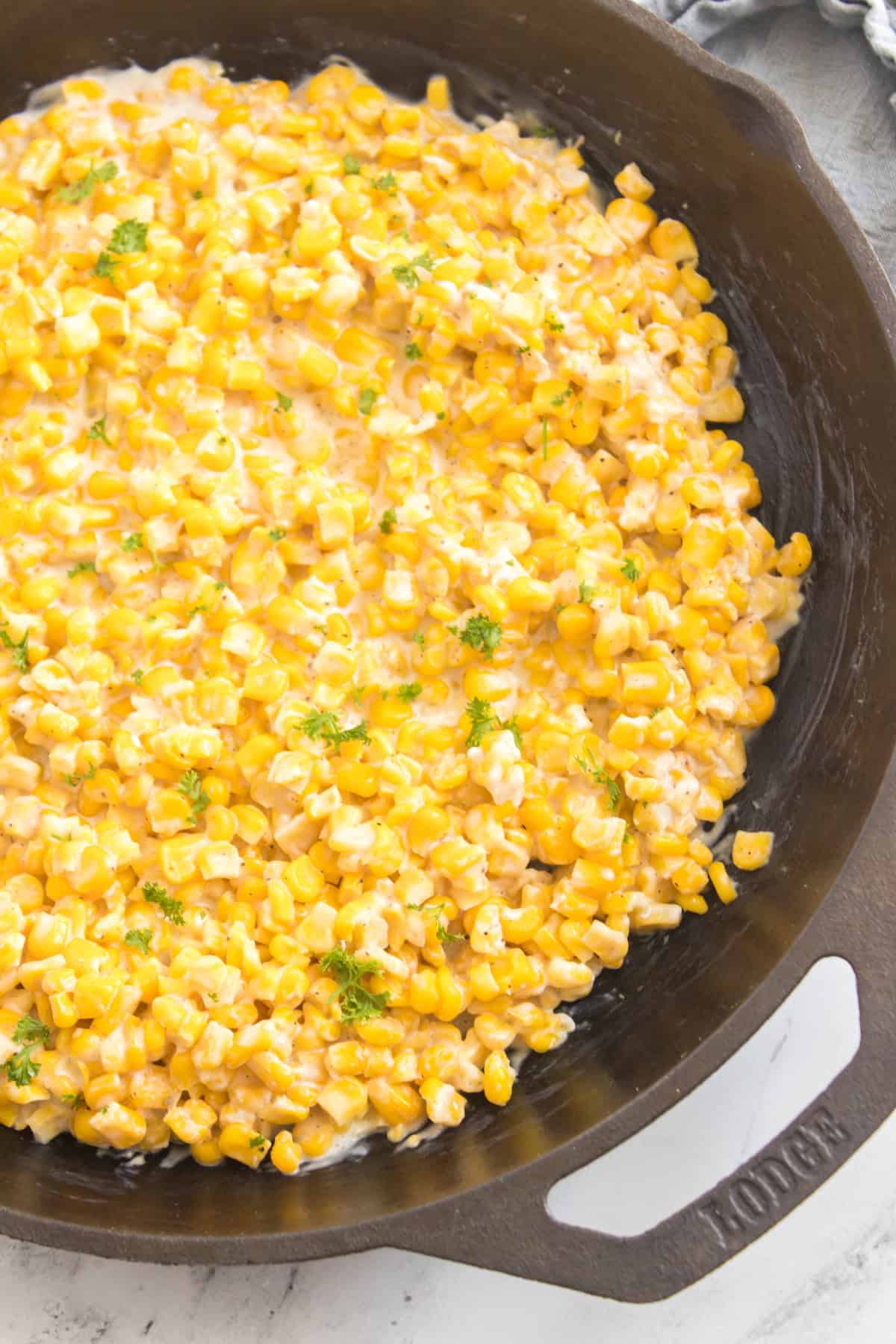 Creamed corn in a cast iron skillet, stirred with a wooden spoon.