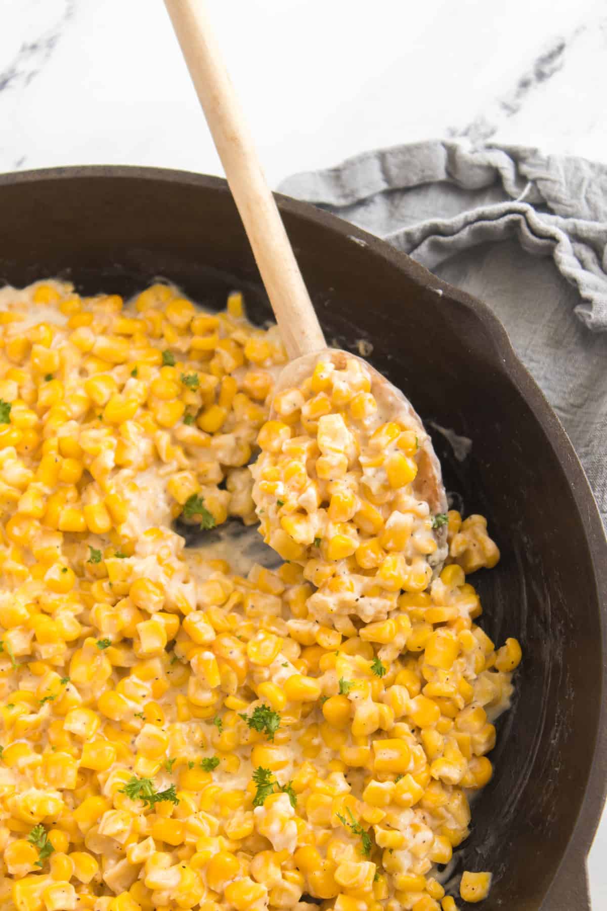 A cast iron pan filled with creamy corn and a wooden spoon inside.