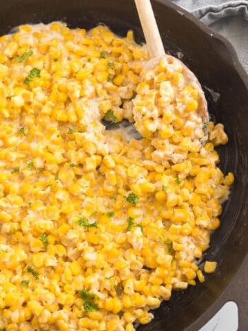 Honey Butter Skillet Corn cooked in a skillet, ready to serve with a wooden spoon scooping it.