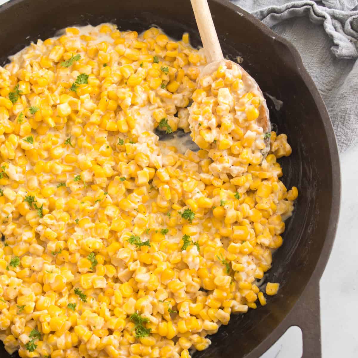 Honey Butter Skillet Corn cooked in a skillet, ready to serve with a wooden spoon scooping it.