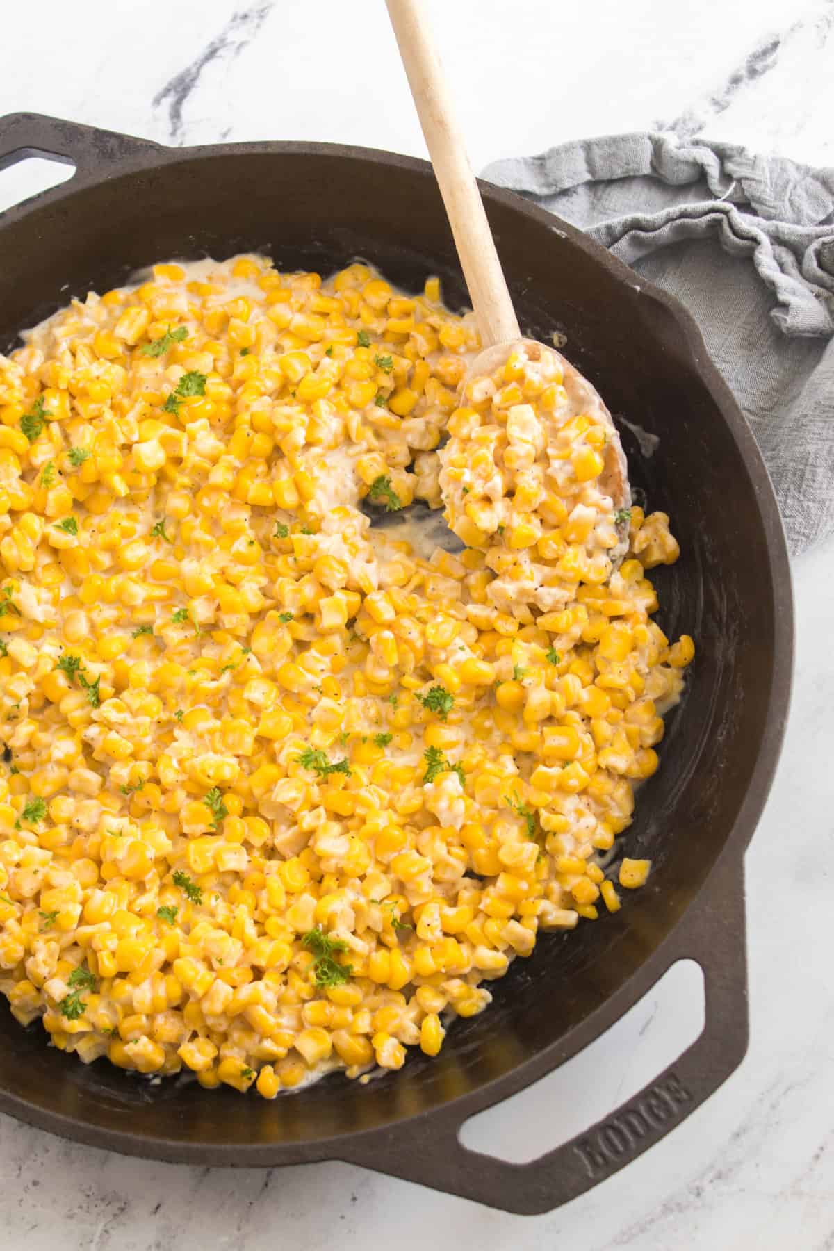Creamy sweet corn cooked in a skillet, ready to serve with a wooden spoon.