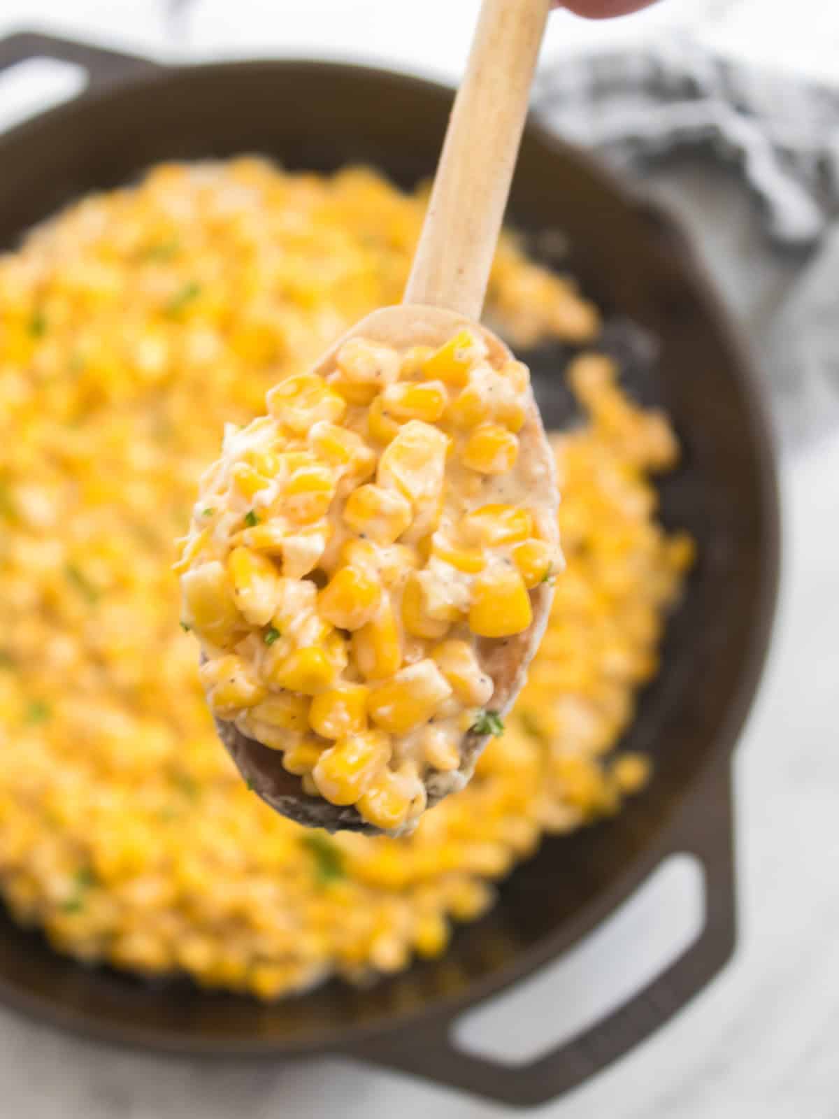 Corn cooked in a skillet, ready to serve with a wooden spoon scooping it.