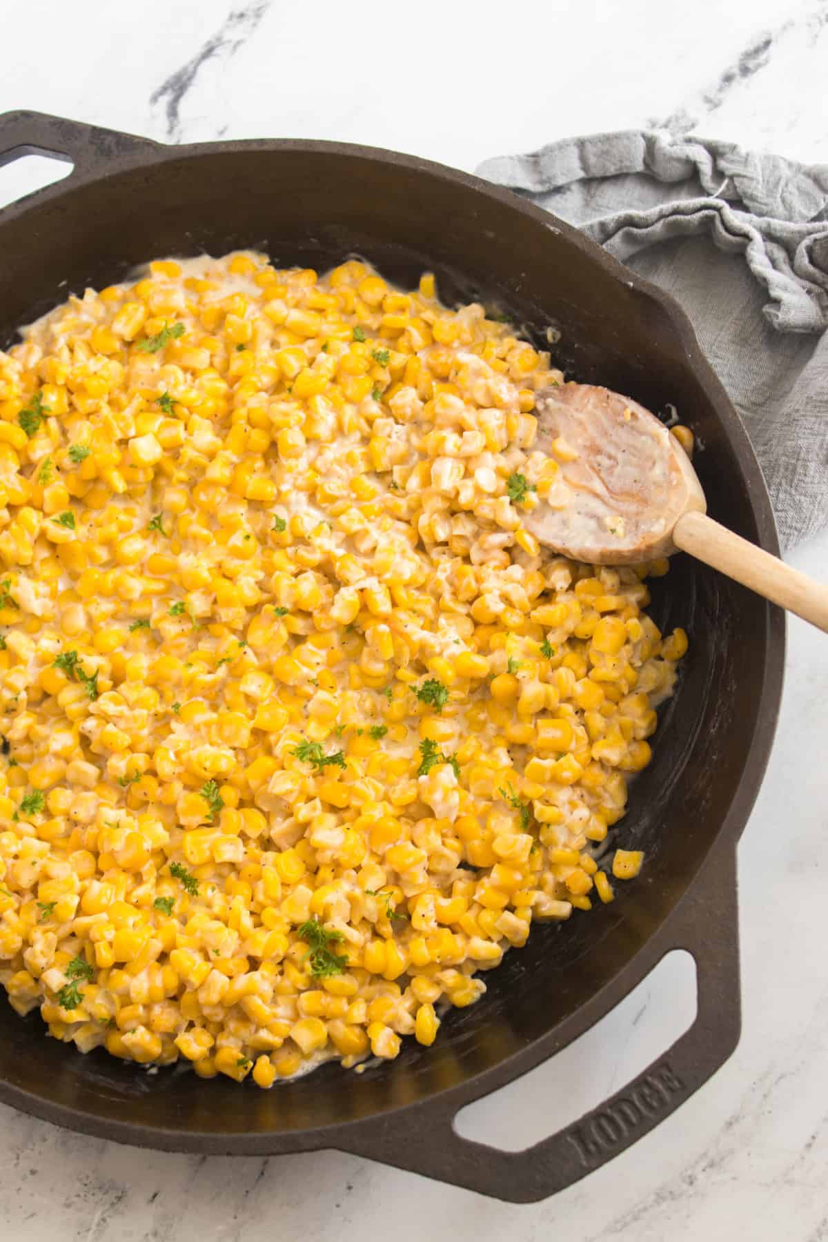 Sweet corn cooked in a skillet, ready to serve with a wooden spoon scooping it.