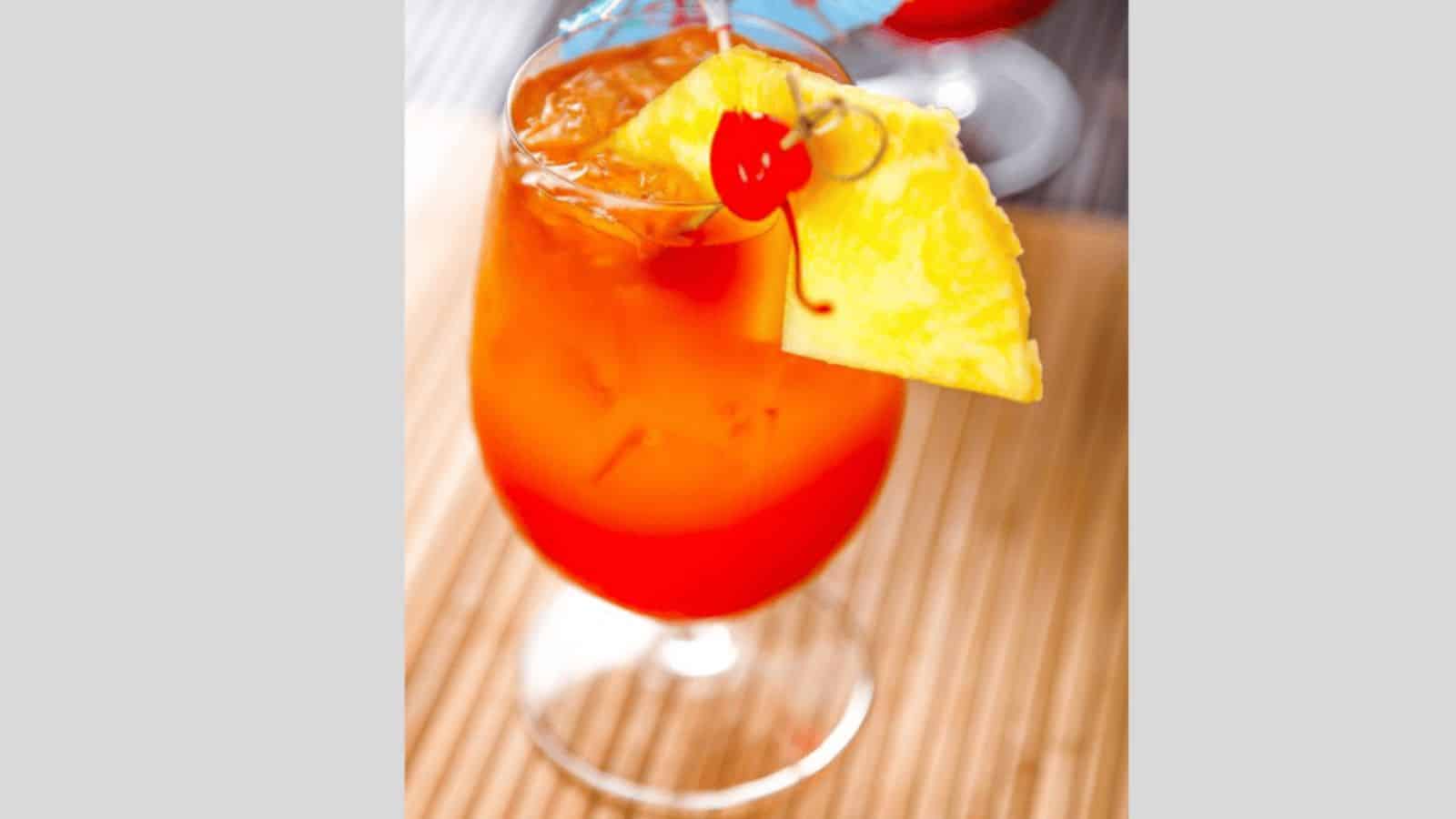 A bahama mama drink garnished with a pineapple slice, cherry, and cocktail umbrella.