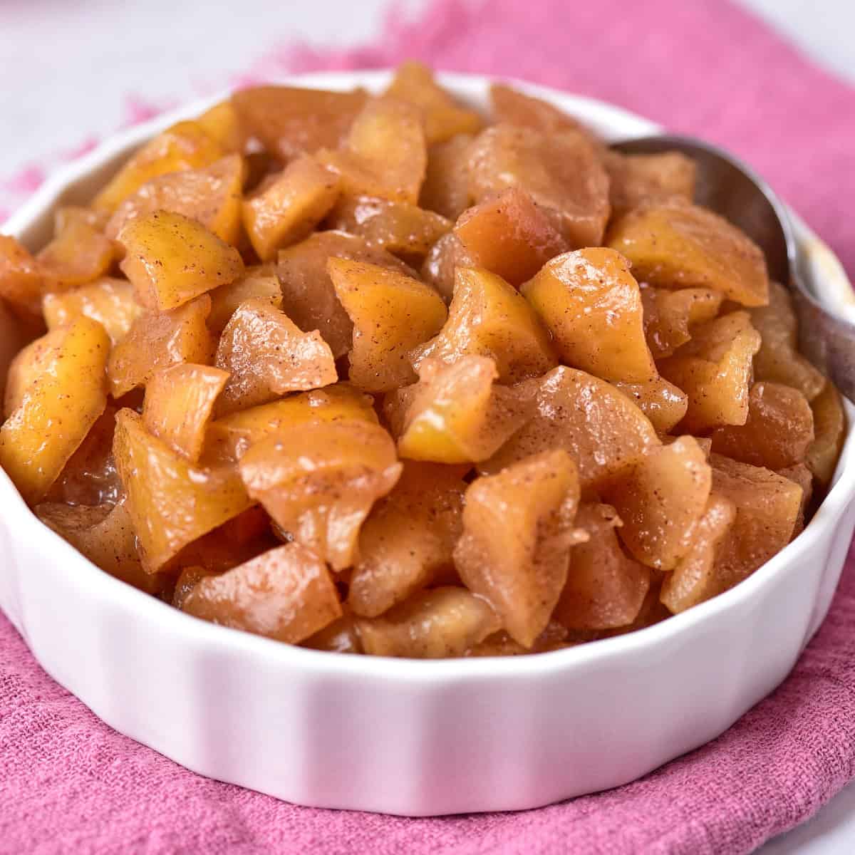 Cooked delicious sweet apples in a bowl, resting on a cozy pink towel.
