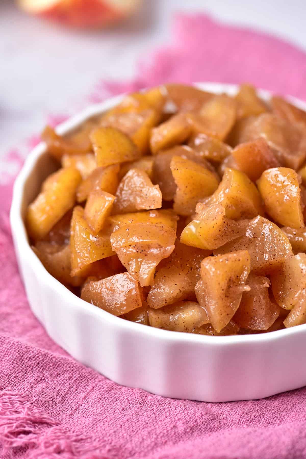 A bowl of cooked sweet apples placed on a soft pink towel.