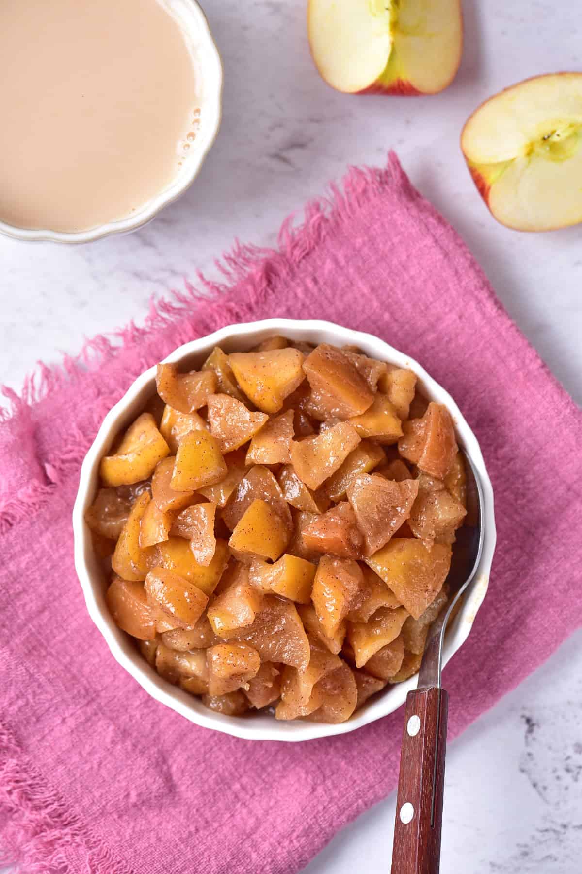 A bowl filled with cooked sweet apples, set on a light pink towel.