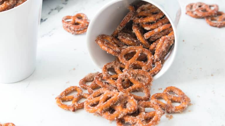 White cup tipped over, spilling out crispy cinnamon pretzels onto a white surface.