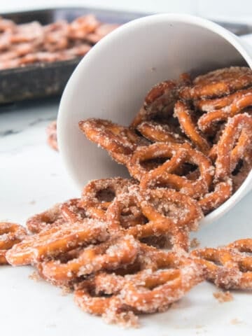 A white cup filled with oven baked cinnamon pretzels in front of a batch cooling on a tray.