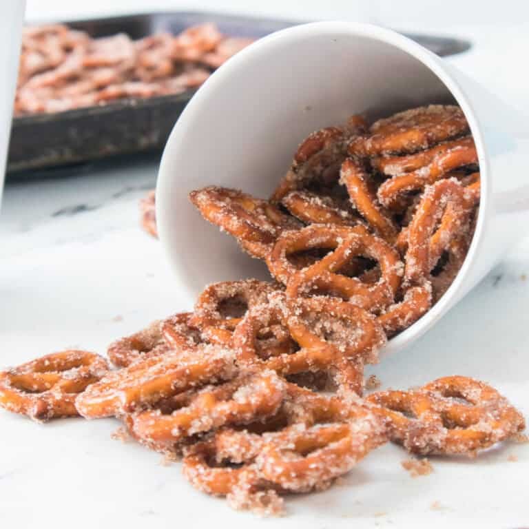 A white cup filled with oven baked cinnamon pretzels in front of a batch cooling on a tray.