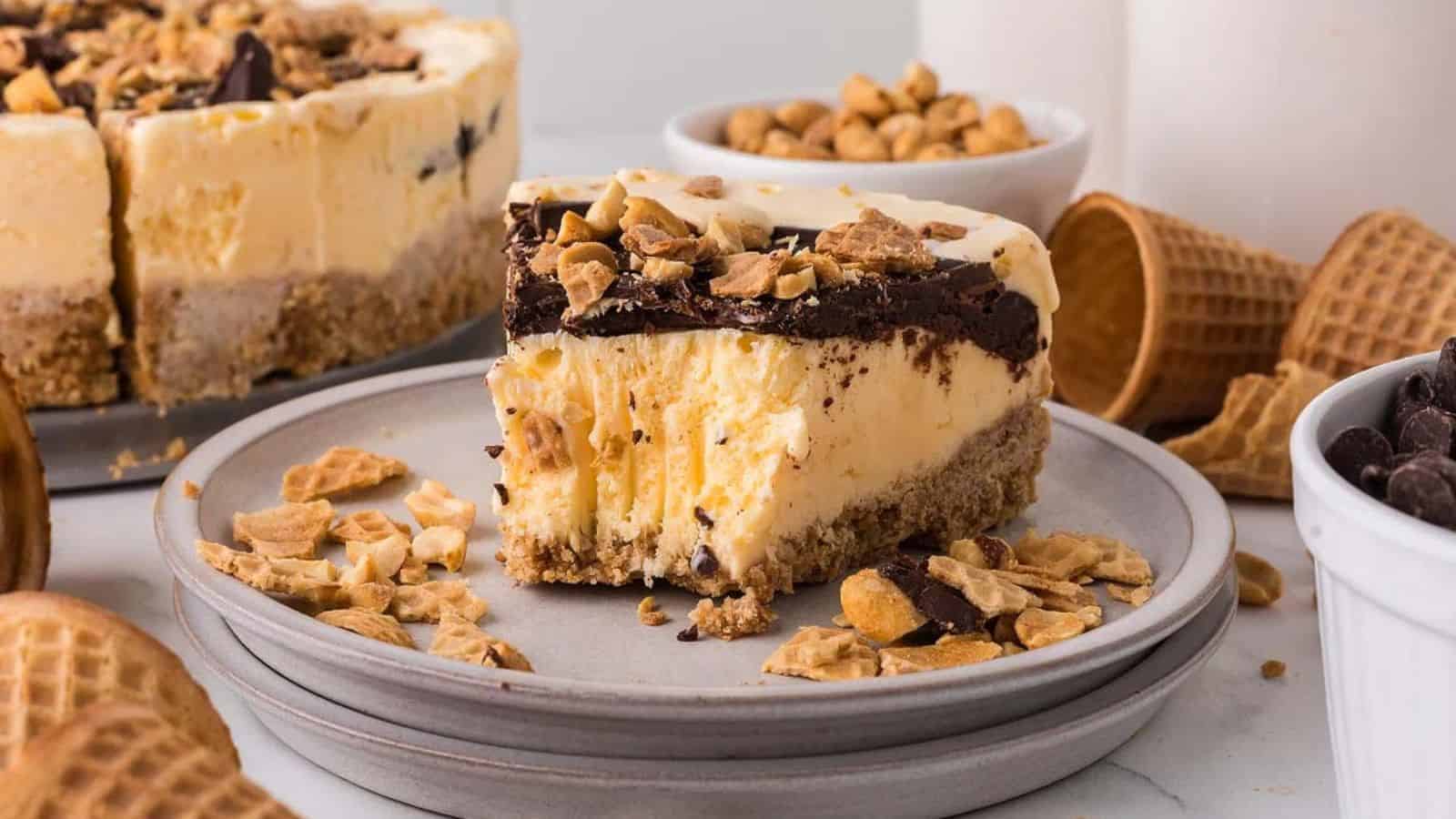 Slice of cake on a plate, topped with chocolate and nuts, surrounded by waffle cones, and bowls of nuts and chocolate chips.