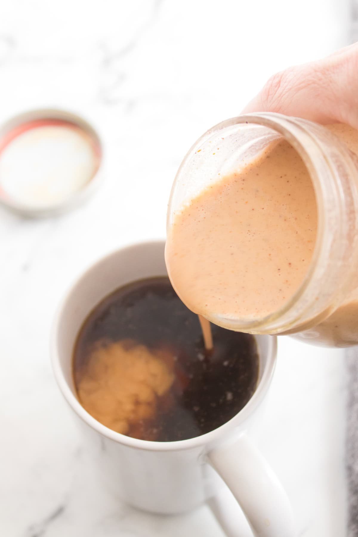 Pouring homemade pumpkin-flavored creamer into a black coffee.