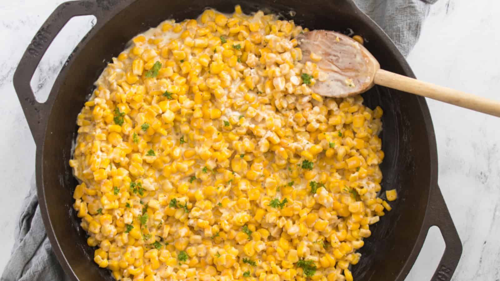 Sweet honey butter corn cooked in a skillet, ready to serve with a wooden spoon scooping it.