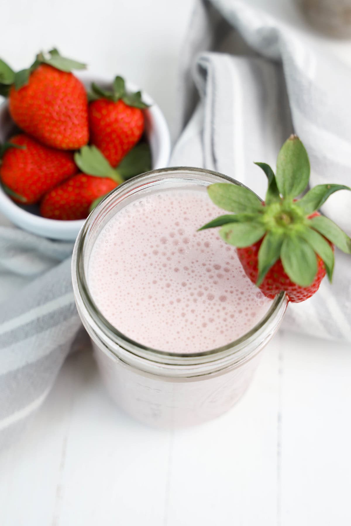 A strawberry banana smoothie served in a tall glass, featuring a strawberry garnishes.